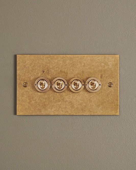 A straight-on view of a 4 gang classic toggle switch in a mottled aged brass finish.