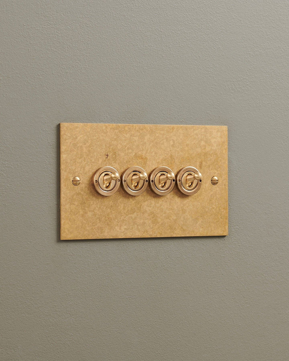 An oblique view of a 4 gang classic toggle switch in a mottled aged brass finish. TEST