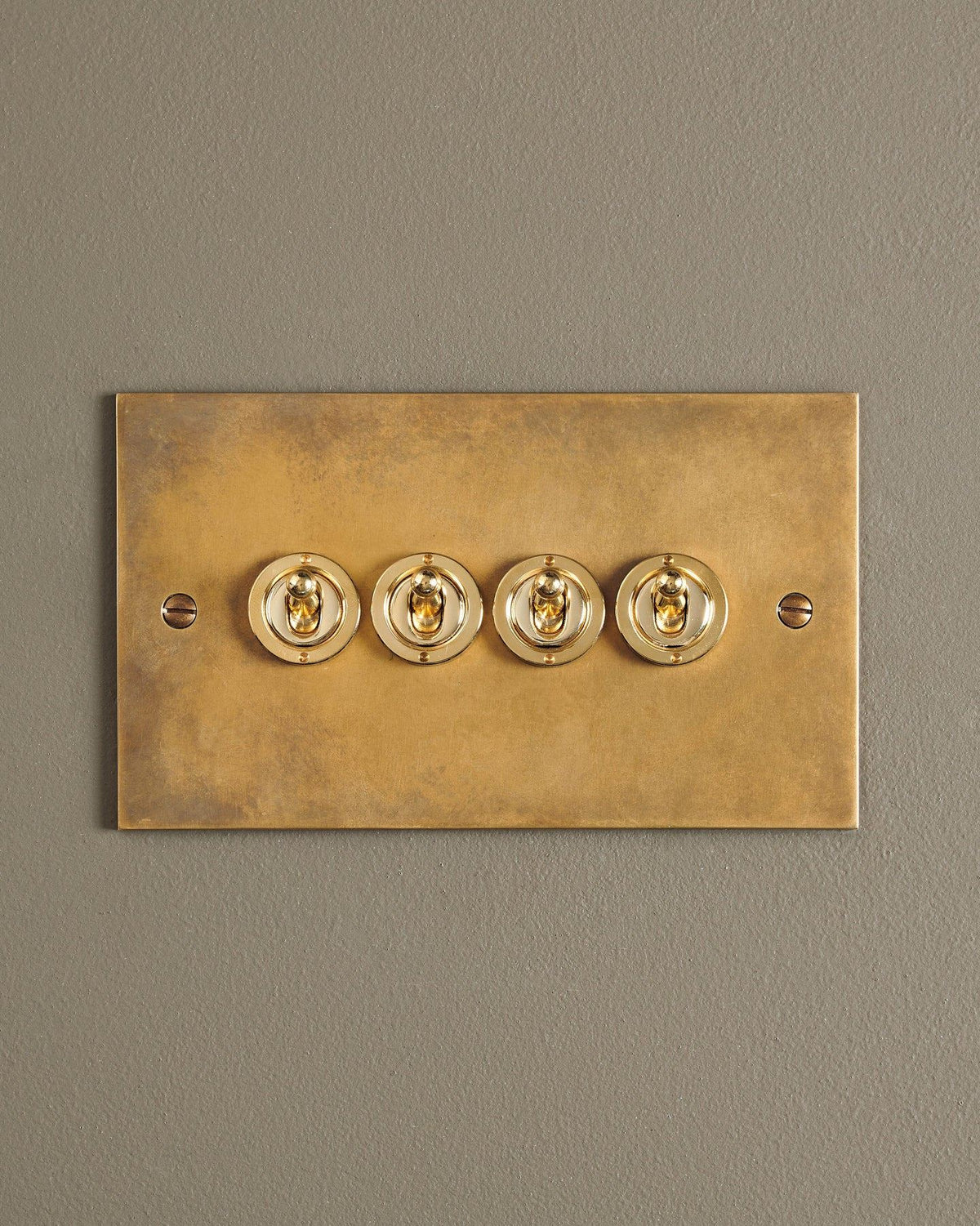 A straight-on view of a 4 gang classic toggle switch in a warm burnished brass finish. TEST