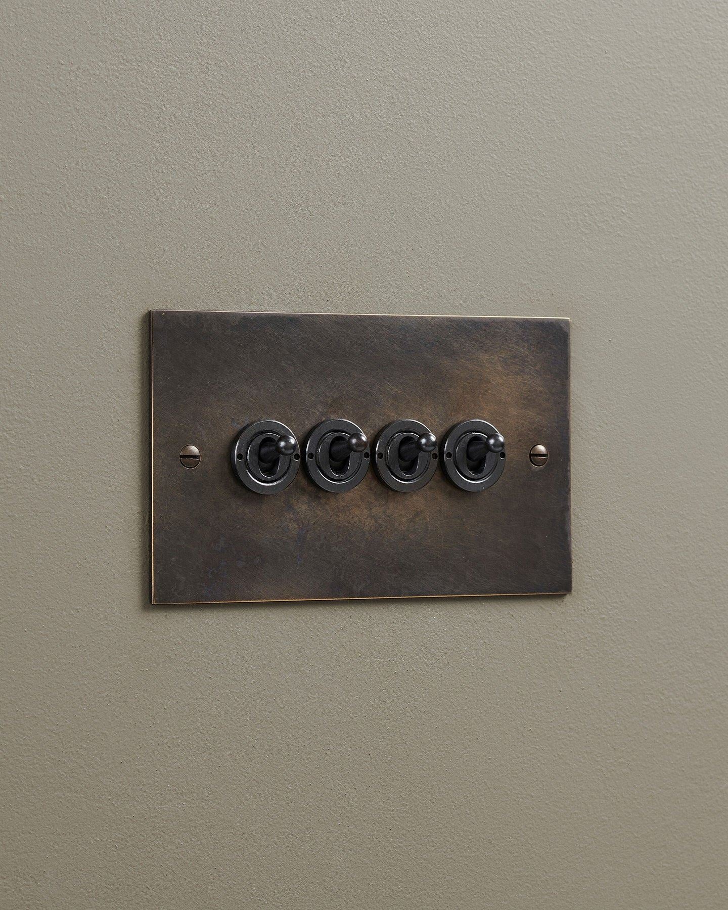 An oblique view of a 4 gang classic toggle switch in a dark oxidised brass finish.