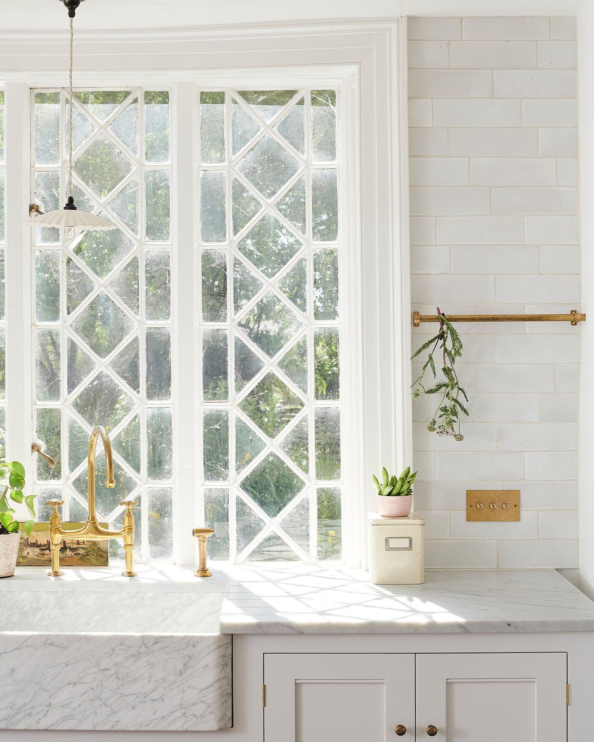 A straight-on view of a 3 gang classic toggle switch in an aged brass finish in a Mediterranean-style kitchen with white painted cupboards, Carrara marble worktop, white metro tiles and original Victorian white leaded windows. | 3 Gang shown TEST