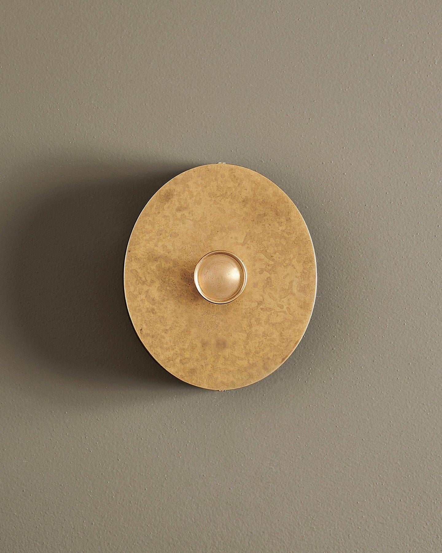 A straight-on view of a 1 gang oval-shaped dimmer switch in a mottled aged brass finish with a black base.