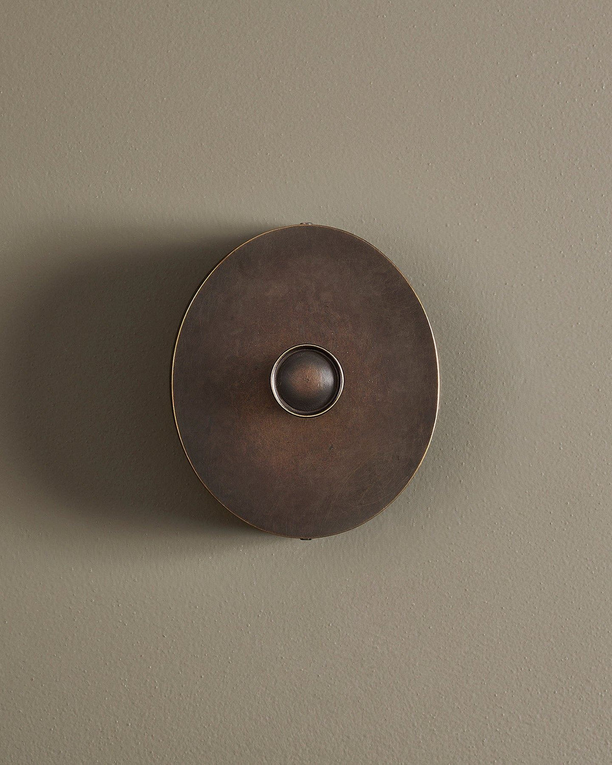 A straight-on view of a 1 gang oval-shaped dimmer switch in a dark oxidised brass finish with a black base. TEST