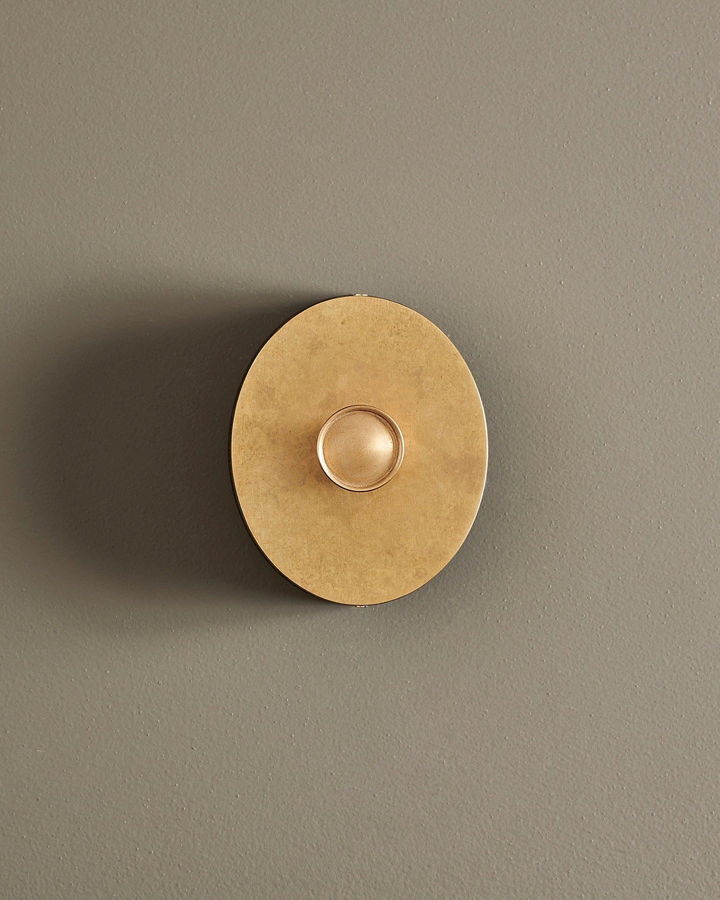 A straight-on view of a small 1 gang oval-shaped dimmer switch in a mottled aged brass finish with a black base.