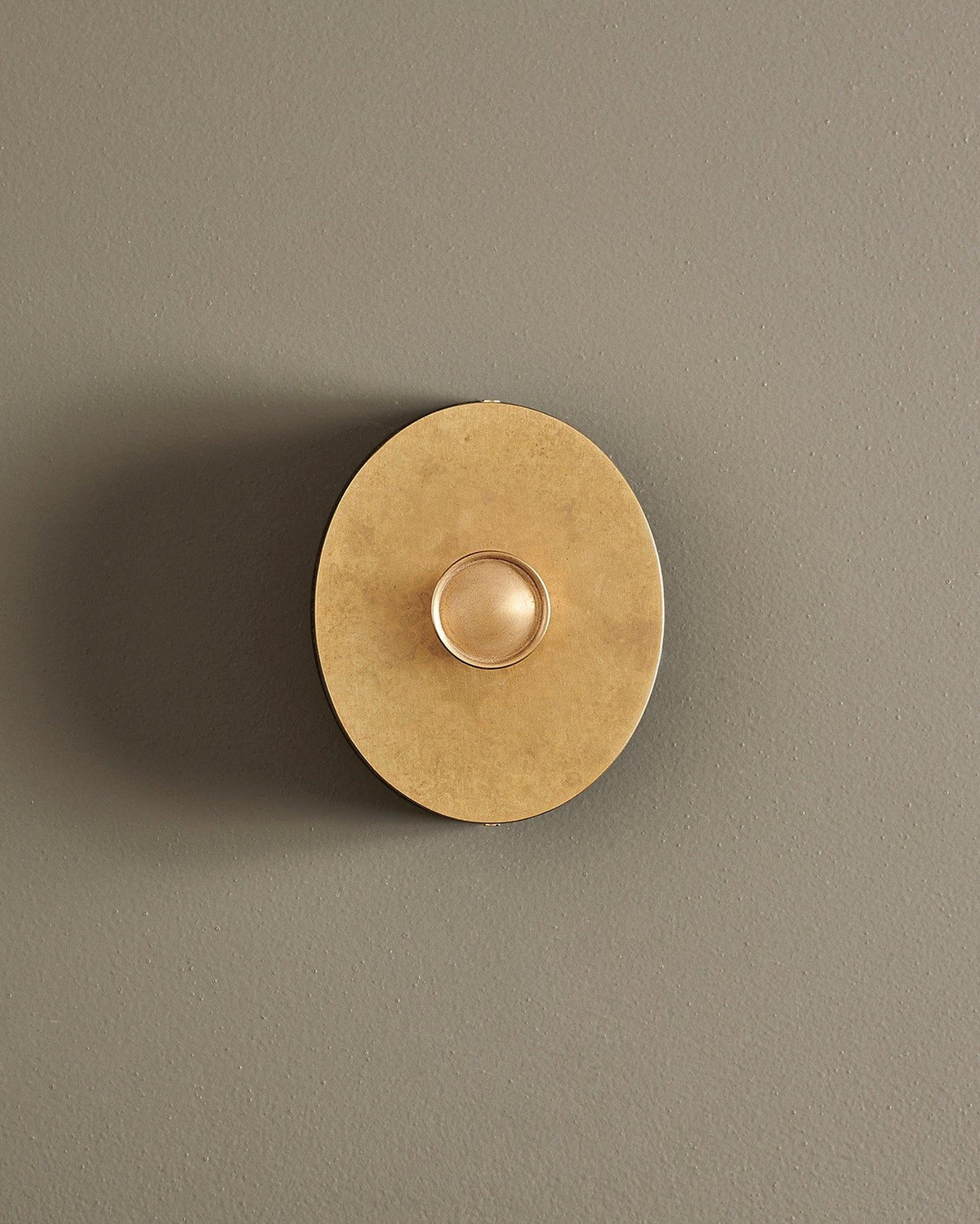 A straight-on view of a small 1 gang oval-shaped dimmer switch in a mottled aged brass finish with a black base. TEST