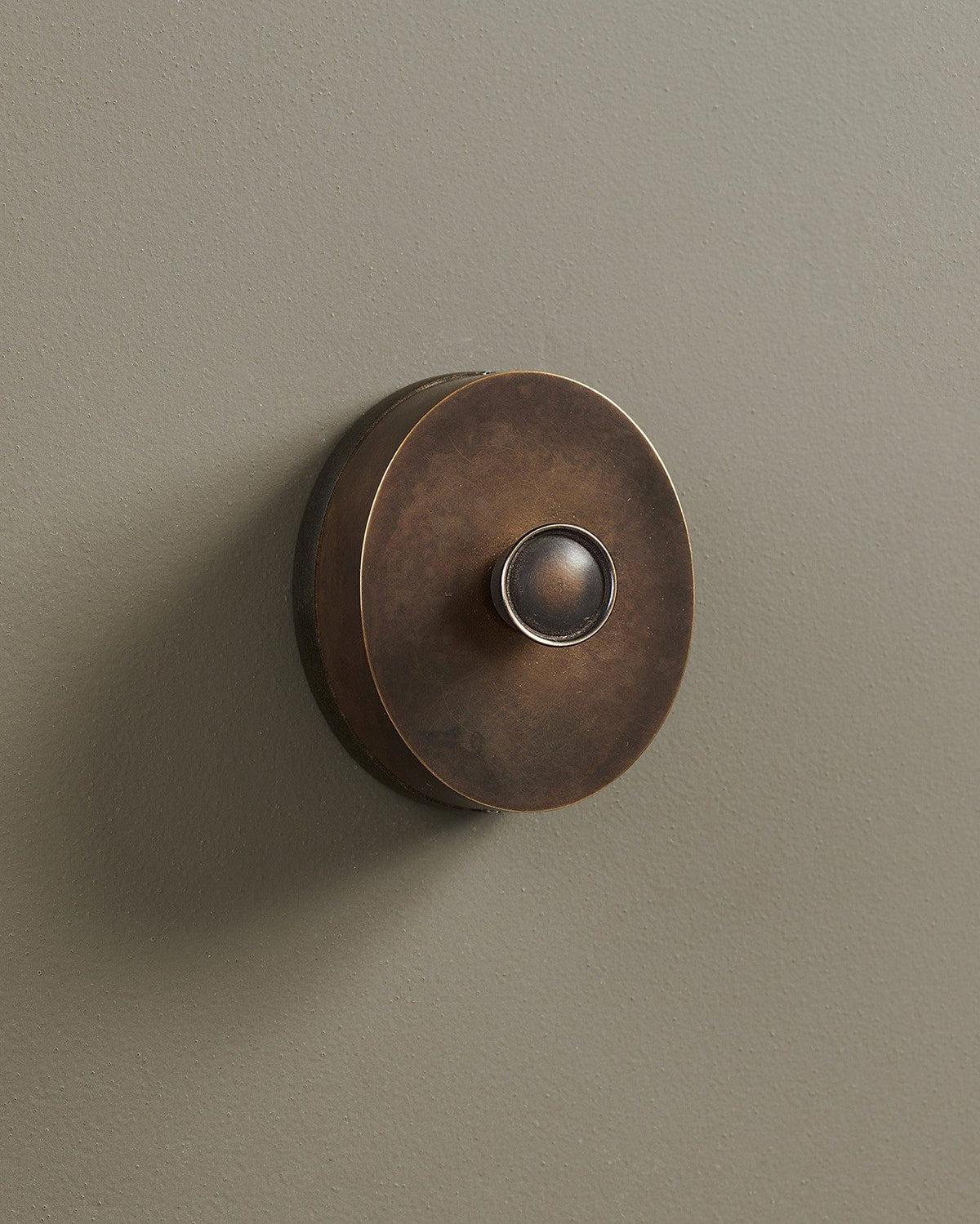 An oblique view of a small 1 gang oval-shaped dimmer switch in a dark oxidised brass finish with a black base. TEST
