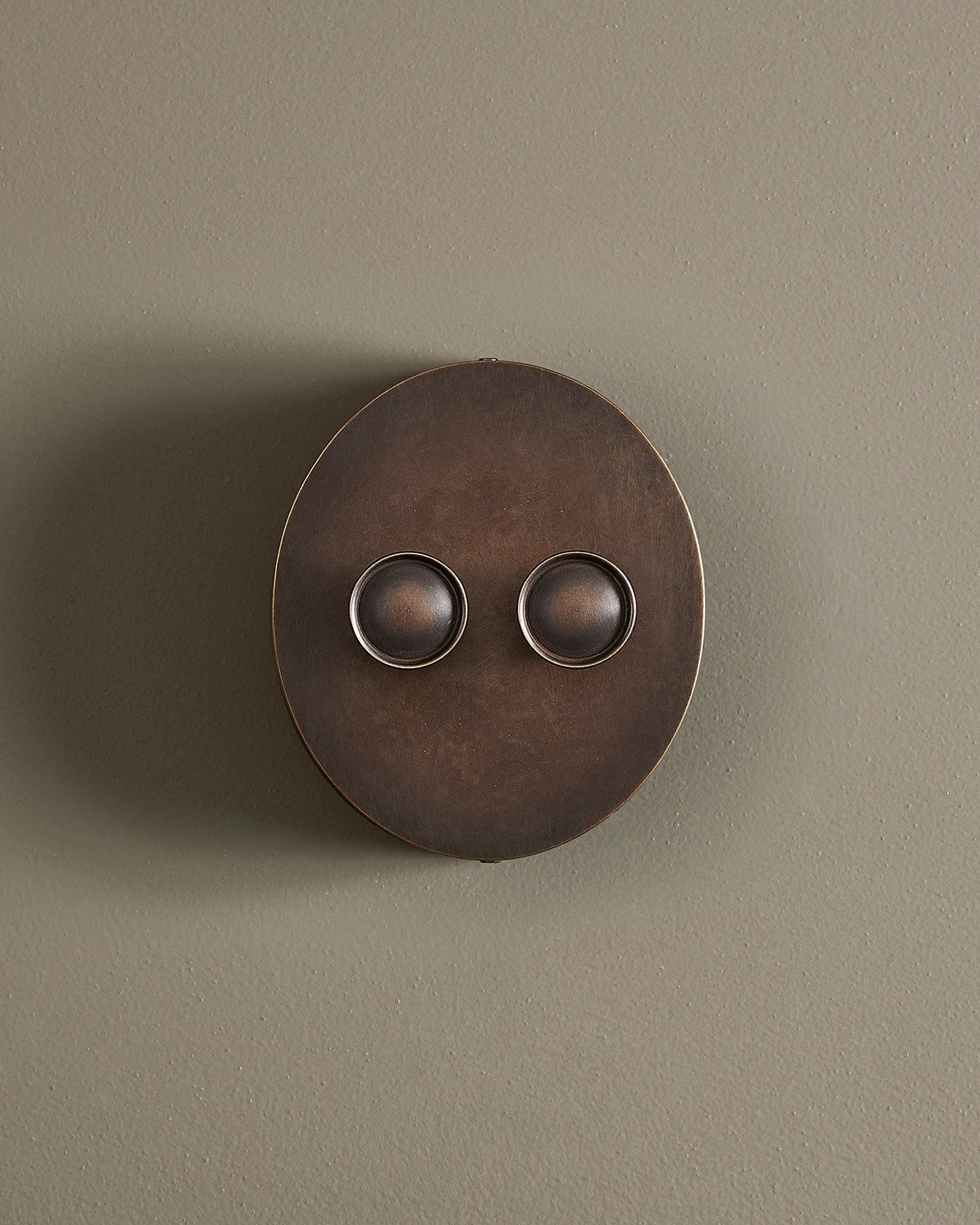 A straight-on view of a 2 gang oval-shaped dimmer switch in a dark oxidised brass finish with a black base.