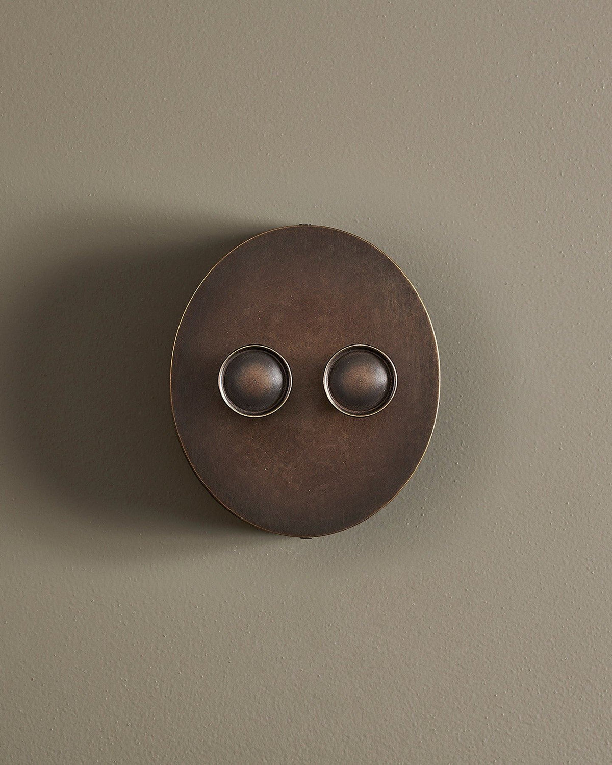 A straight-on view of a 2 gang oval-shaped dimmer switch in a dark oxidised brass finish with a black base. TEST