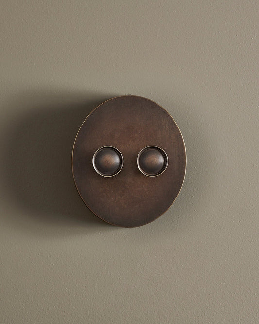 A straight-on view of a 2 gang oval-shaped dimmer switch in a dark oxidised brass finish with a black base.