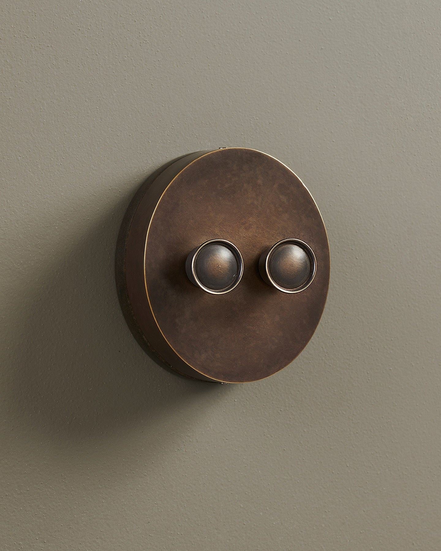 An oblique view of a 2 gang oval-shaped dimmer switch in a dark oxidised brass finish with a black base.