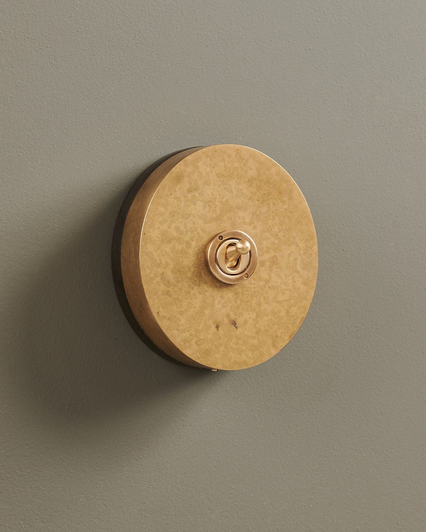 An oblique view of a 1 gang oval-shaped toggle switch in a mottled aged brass finish with a black base.