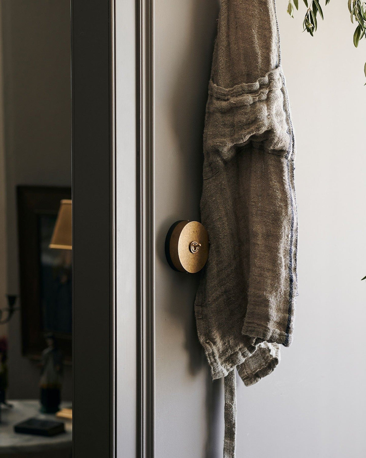 A 1 gang oval-shaped toggle switch in aged brass on a grey wall, hiding behind a vintage linen apron. | 1 Gang shown TEST