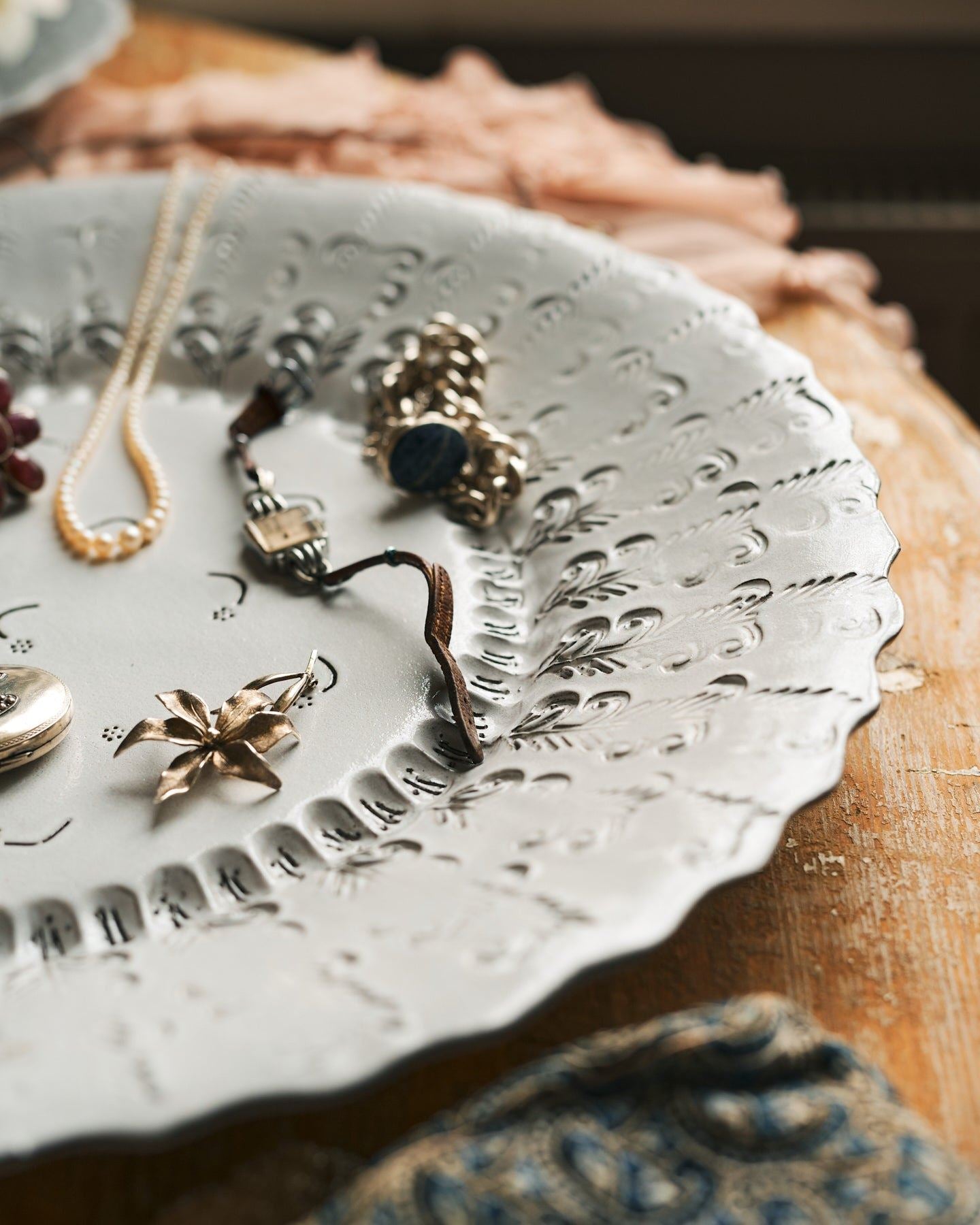 A close-up view of a large bohemian-style glossy white ceramic platter with a scalloped rim and delicate impressions and surface patterns.