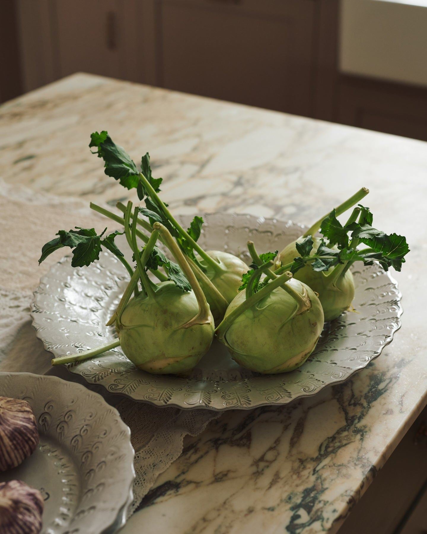 Organic green kohlrabi on a large handmade bohemian-style glossy white ceramic platter with a scalloped rim.