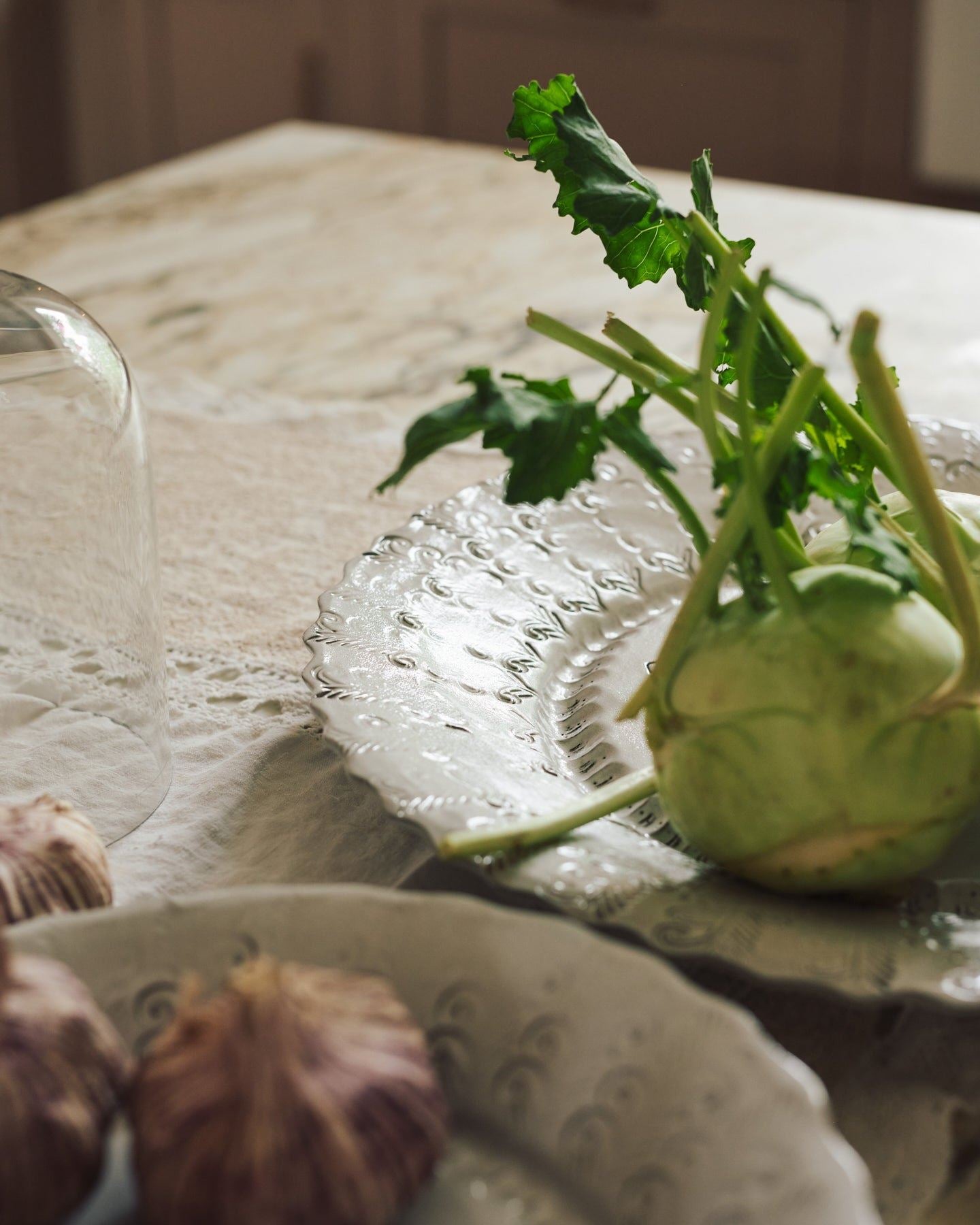 A close-up view of kohlrabi and garlic heads on a large handmade bohemian-style glossy white ceramic platter with a scalloped rim.
