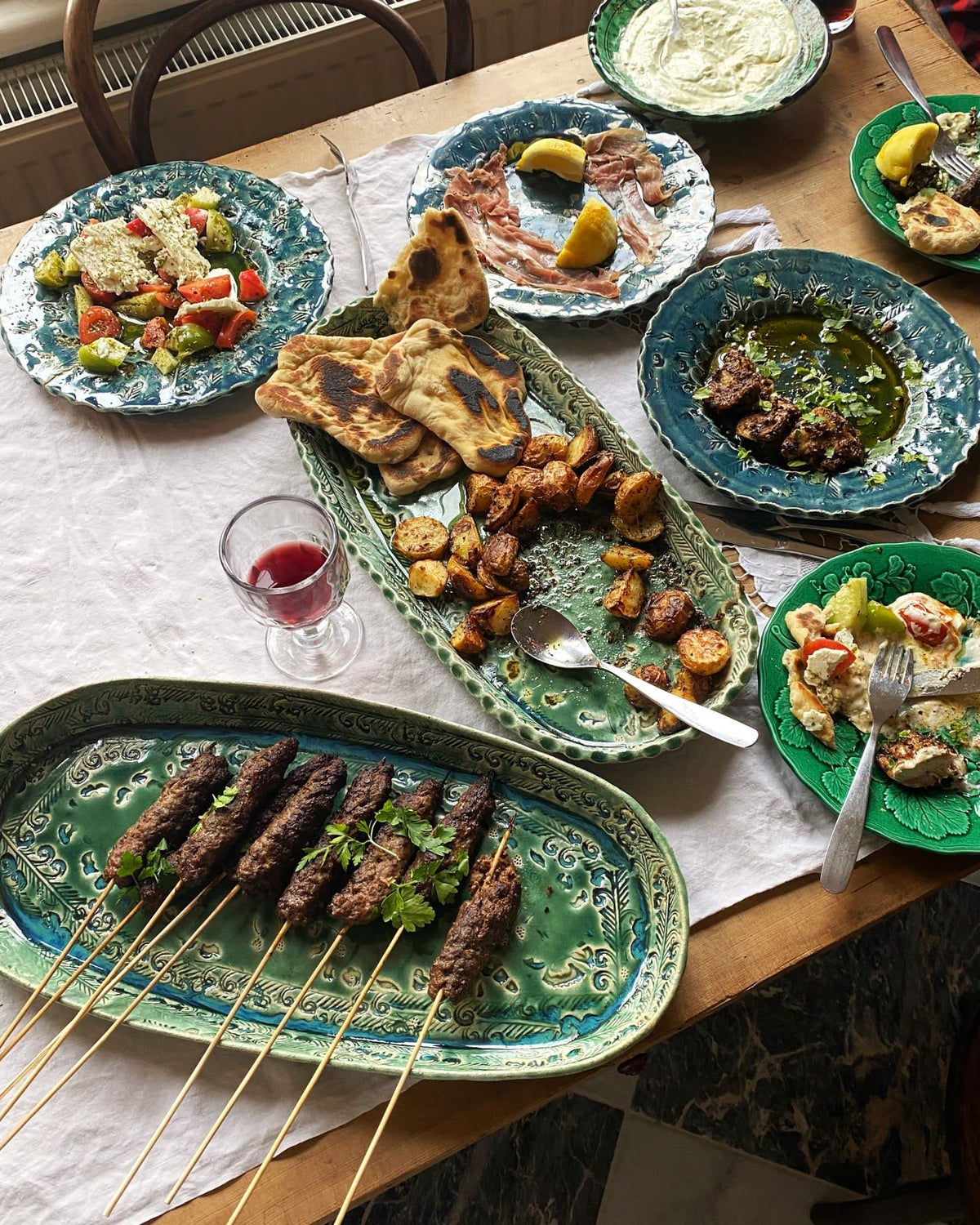 Several oval and round handmade bohemian-style ceramic platters set at a table with a vintage lace tablecloth and a variety of Mediterranean foods. TEST