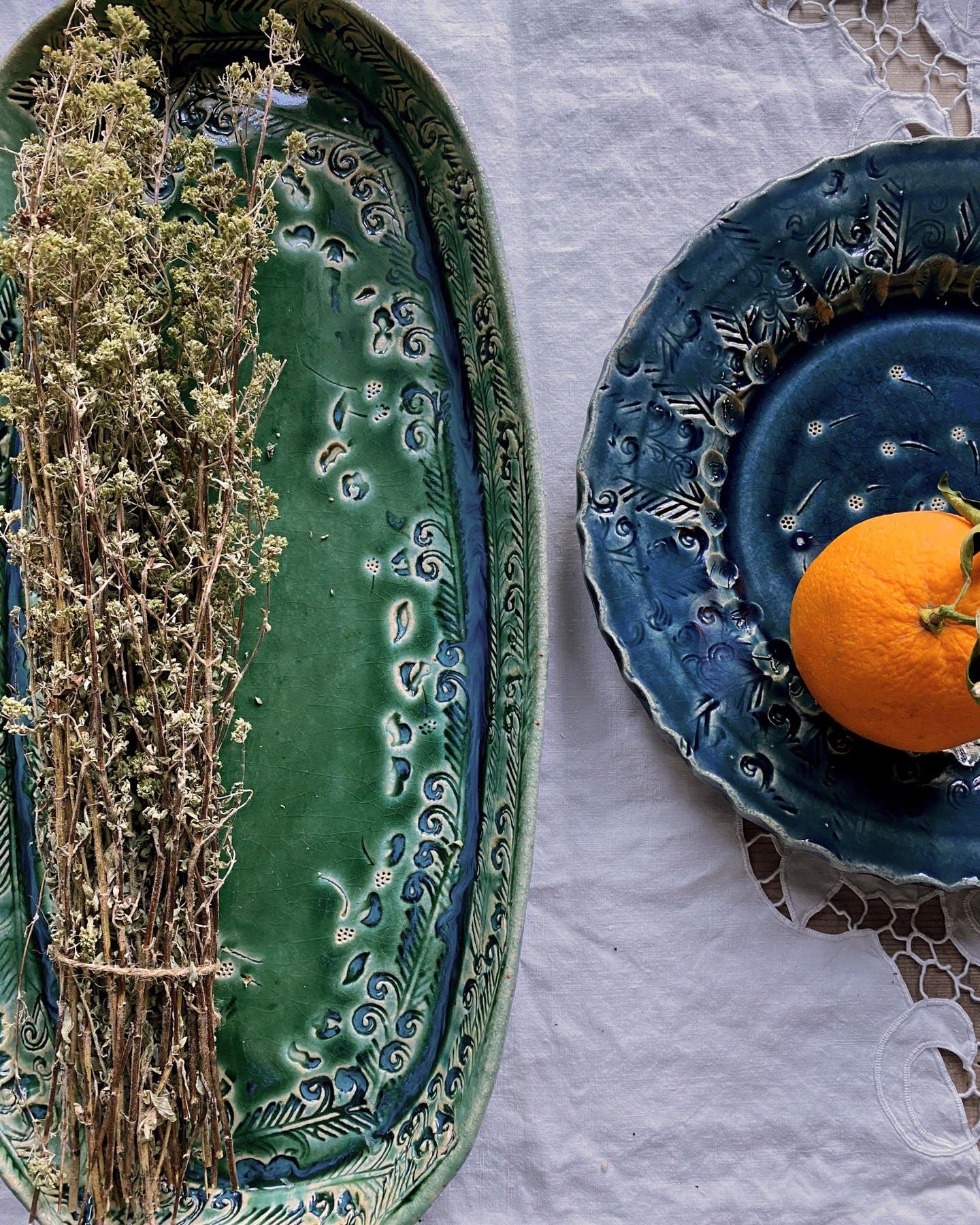 An overhead view of a green oval-shaped ceramic platter and a blue round-shaped ceramic platter with a single orange on top.