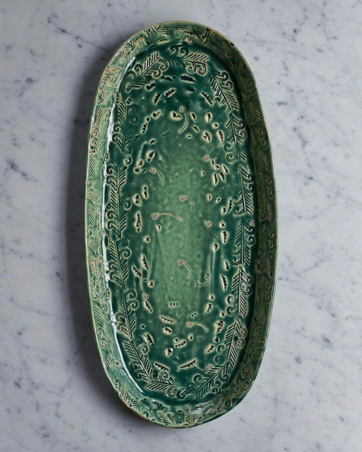 An overhead view of an oval-shaped handmade bohemian-style green ceramic platter with delicate impressions and surface patterns.
