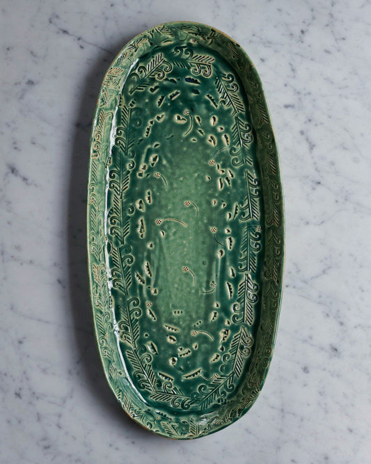 An overhead view of an oval-shaped handmade bohemian-style green ceramic platter with delicate impressions and surface patterns.