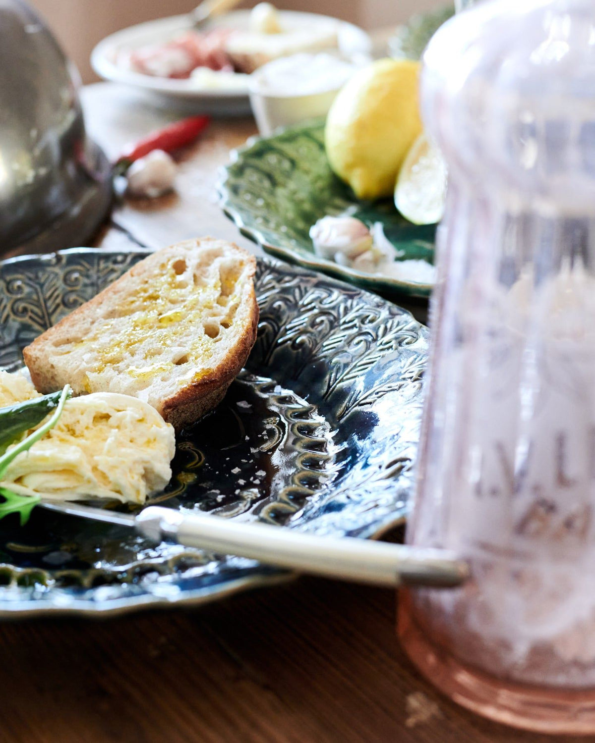 A close-up view of a round handmade bohemian-style blue ceramic platter with vintage silverware, cheese and homemade bread. TEST