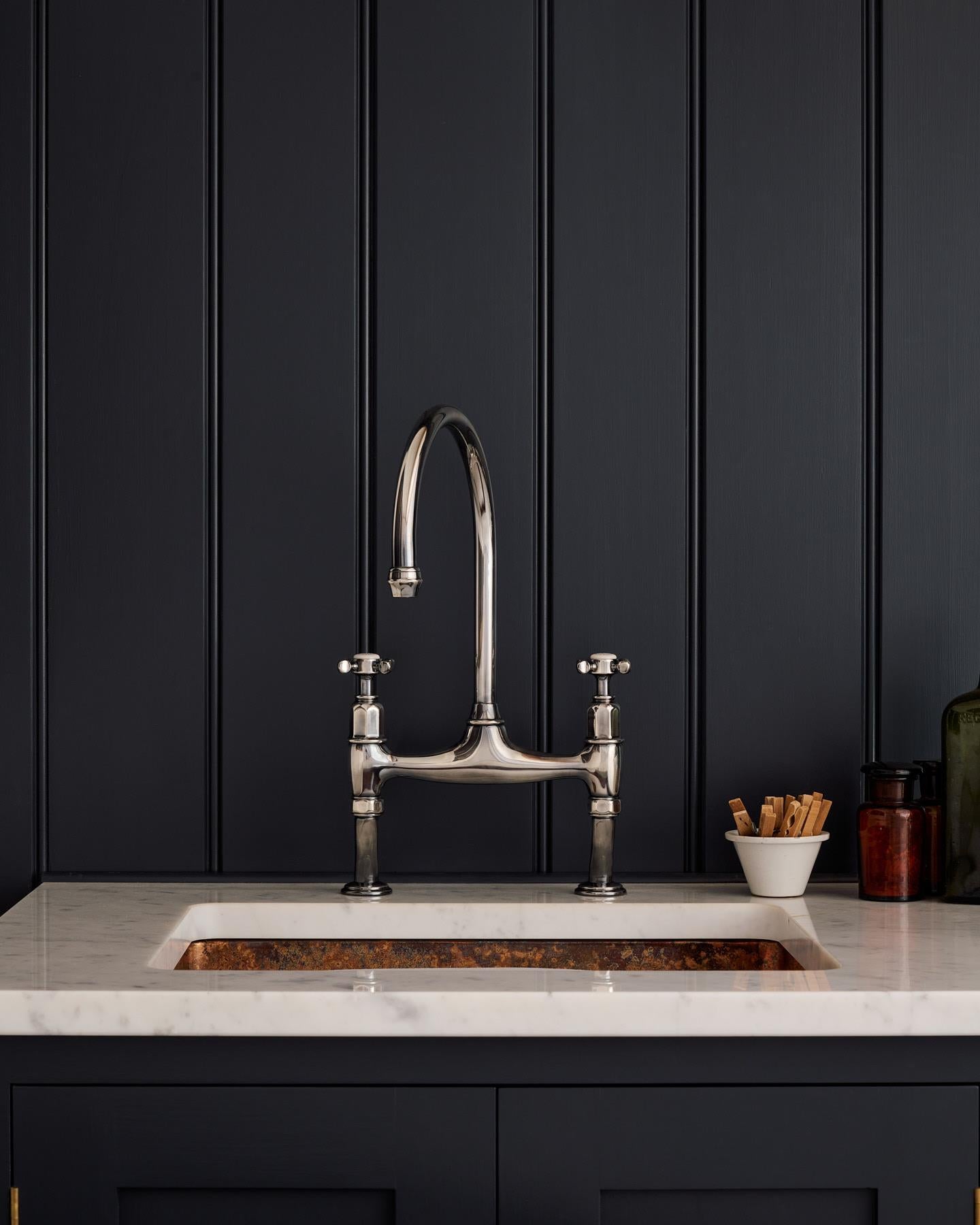 A straight-on view of a traditional-style tarnished silver mixer tap with crosshead handles in a classic utility kitchen with a Carrara marble worktop and deep blue painted cupboards and tongue and groove panelling.