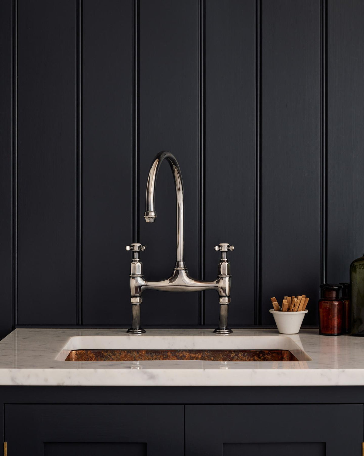A straight-on view of a traditional-style tarnished silver mixer tap with crosshead handles in a classic utility kitchen with a Carrara marble worktop and deep blue painted cupboards and tongue and groove panelling. TEST