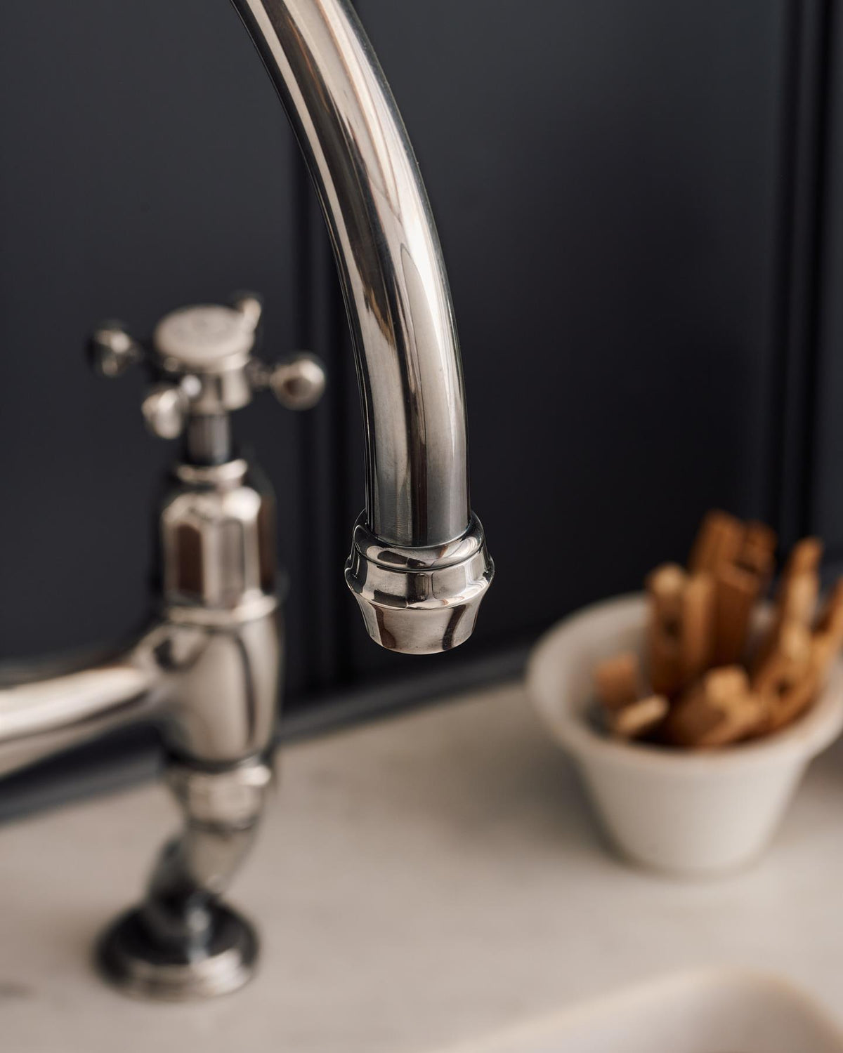 A close-up view of the spout of a traditional-style tarnished silver mixer tap with crosshead handles. TEST