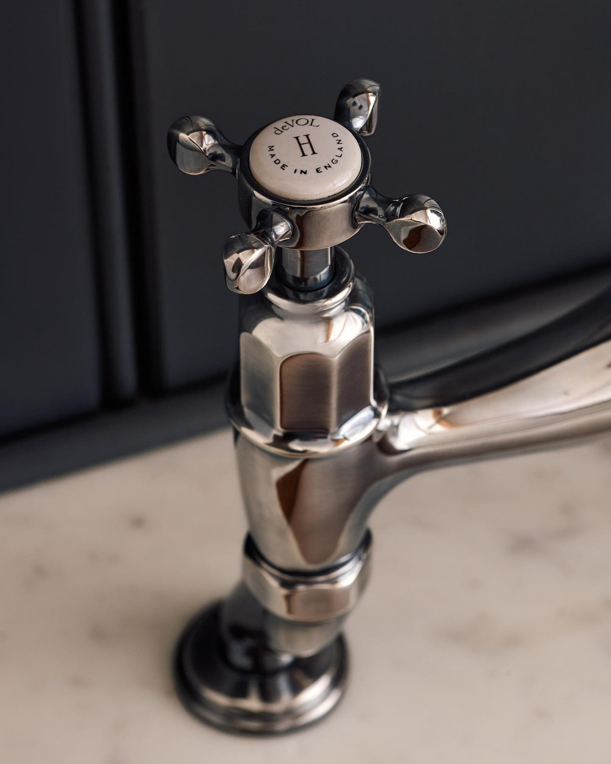 A close-up view of a crosshead handle of a traditional-style tarnished silver mixer tap. An 'H' can be seen in the centre of the handle with the words 'deVOL' and 'Made in England' around the perimeter. TEST