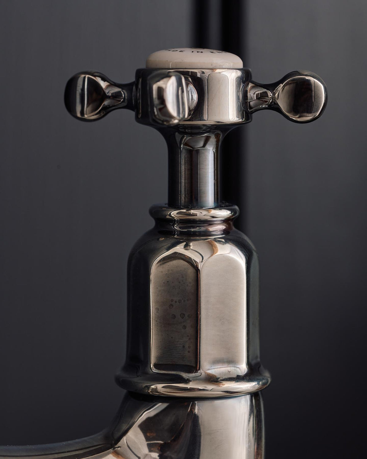 A close-up profile view of a crosshead handle of a traditional-style tarnished silver mixer tap. TEST