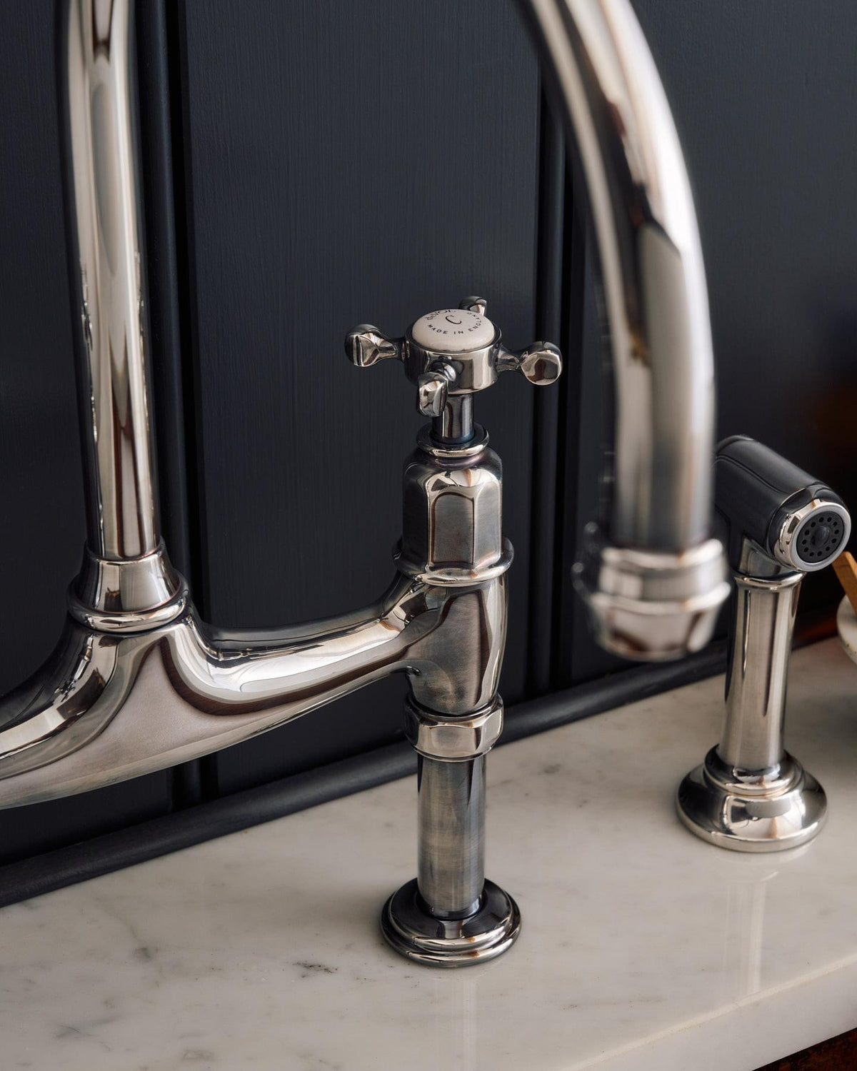 A close-up view of the spout of a traditional-style tarnished silver mixer tap with crosshead handles. TEST