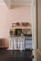 A decorative corner of a light pastel-blue classic kitchen’s cooker run with a beautiful turquoise marble worktop. The London apartment has high ceilings, worn black painted floorboards, small decorative splashback mirrors, intricate cornices, and is styled with the customer's collection of antiques.