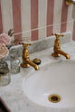 A closer look at the small painter’s black Victorian washstand with aged brass Mayan tap in a chic bathroom featuring pink and white tiled walls.