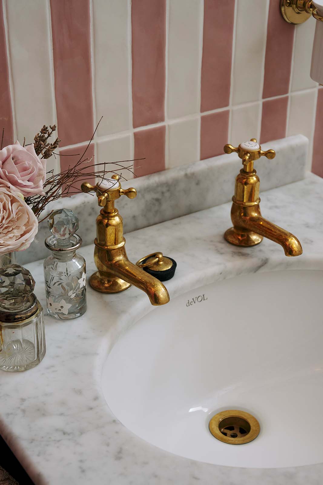 A closer look at the small painter’s black Victorian washstand with aged brass Mayan tap in a chic bathroom featuring pink and white tiled walls.
