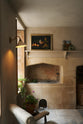 In the quiet corner of a rustic basement kitchen with sandy-coloured walls and ceiling, original Georgian detailing, cream doors and panelling with chipped paintwork and a worn stone floor. An heirloom wall light fits perfectly at home in the ancient and preserved wall.