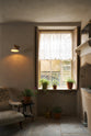 In the quiet corner of a rustic basement kitchen with sandy-coloured walls and ceiling, original Georgian detailing, cream doors and panelling with chipped paintwork and a worn stone floor. An heirloom wall light gently illuminated the ancient and preserved wall.