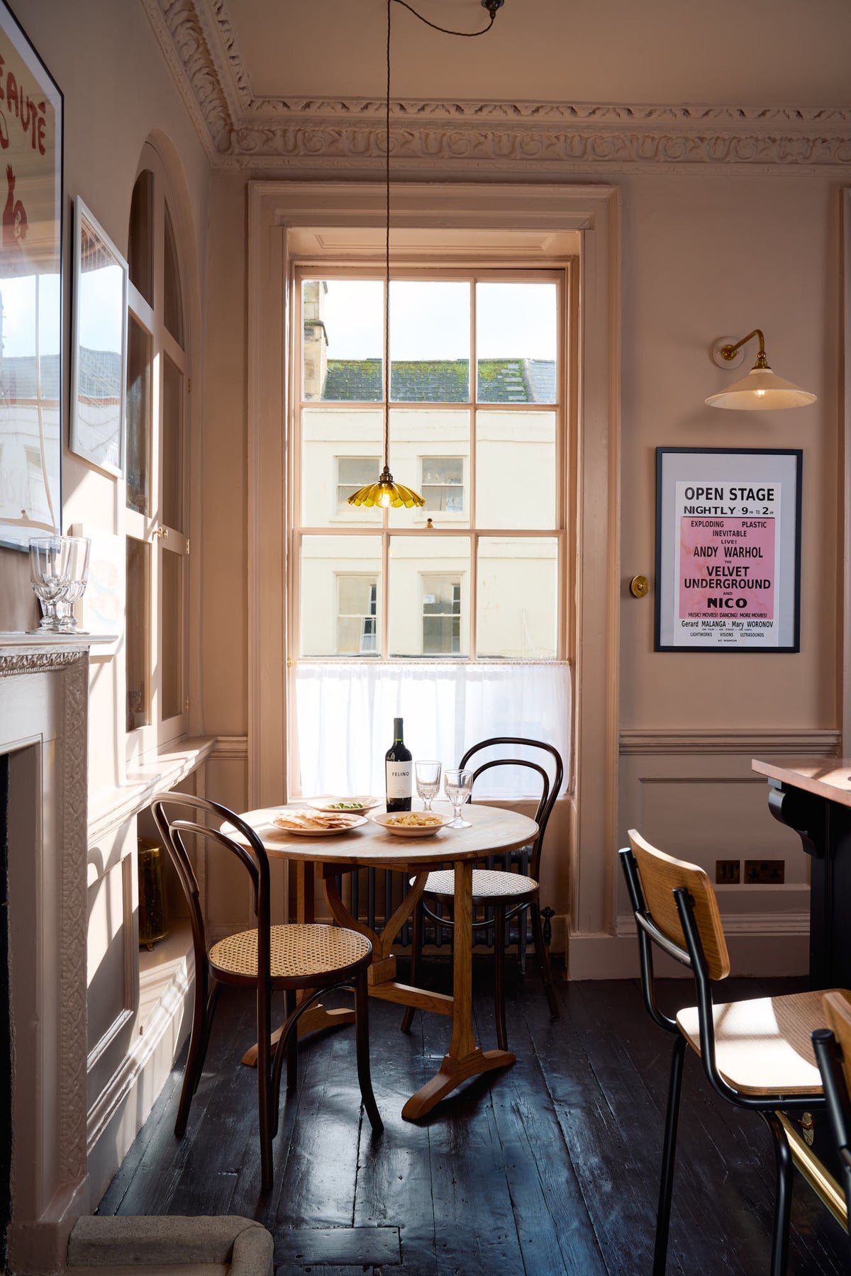 A quiet corner of a bold and dramatic Haberdasher’s kitchen features a deVOL petite vineyard table, Bentwood café chairs, and a petite frilly chartreuse light. Adorned with a delicious bottle of wine, drinking glasses, hors d’oeuvres, quirky framed illustrations and posters, and labelled glass jars, this space creates a local bistro bar atmosphere in Manhattan.