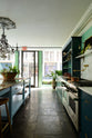 A stunning, Bond Street blue kitchen features a cooker run with Arabescato marble worktop and splashback, and a bank of open pantry larder. The room features a stunning mix of colours and character, accentuated by elegant antiques such as a crystal chandelier, a collection of colourful drinking glasses, and an aged brass pot filler.