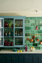 A closer look at a stunning, Bond Street blue kitchen features a sink run with Arabescato marble worktop, and a large wall cupboard. The room features a stunning mix of colours and character, accentuated by elegant antiques such as artisan ceramics, colourful glass pendant lights, aged brass rails with copper pans, and deVOL Emerald green London splashback tiles.