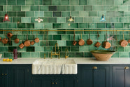 A stunning, Bond Street blue kitchen features a sink and cooker run with Arabescato marble worktop, and an aged brass ionian tap. The room features a stunning mix of colours and character, accentuated by elegant antiques such as colourful glass pendant lights, aged brass rails with copper pans, and deVOL Emerald green London splashback tiles.