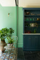 A quiet corner of a stunning, Bond Street blue kitchen features a bank of open pantry larder. The room features a stunning mix of colours and character, accentuated by elegant antiques such as a collection of colourful drinking glasses, potted plants, and artisan ceramics.