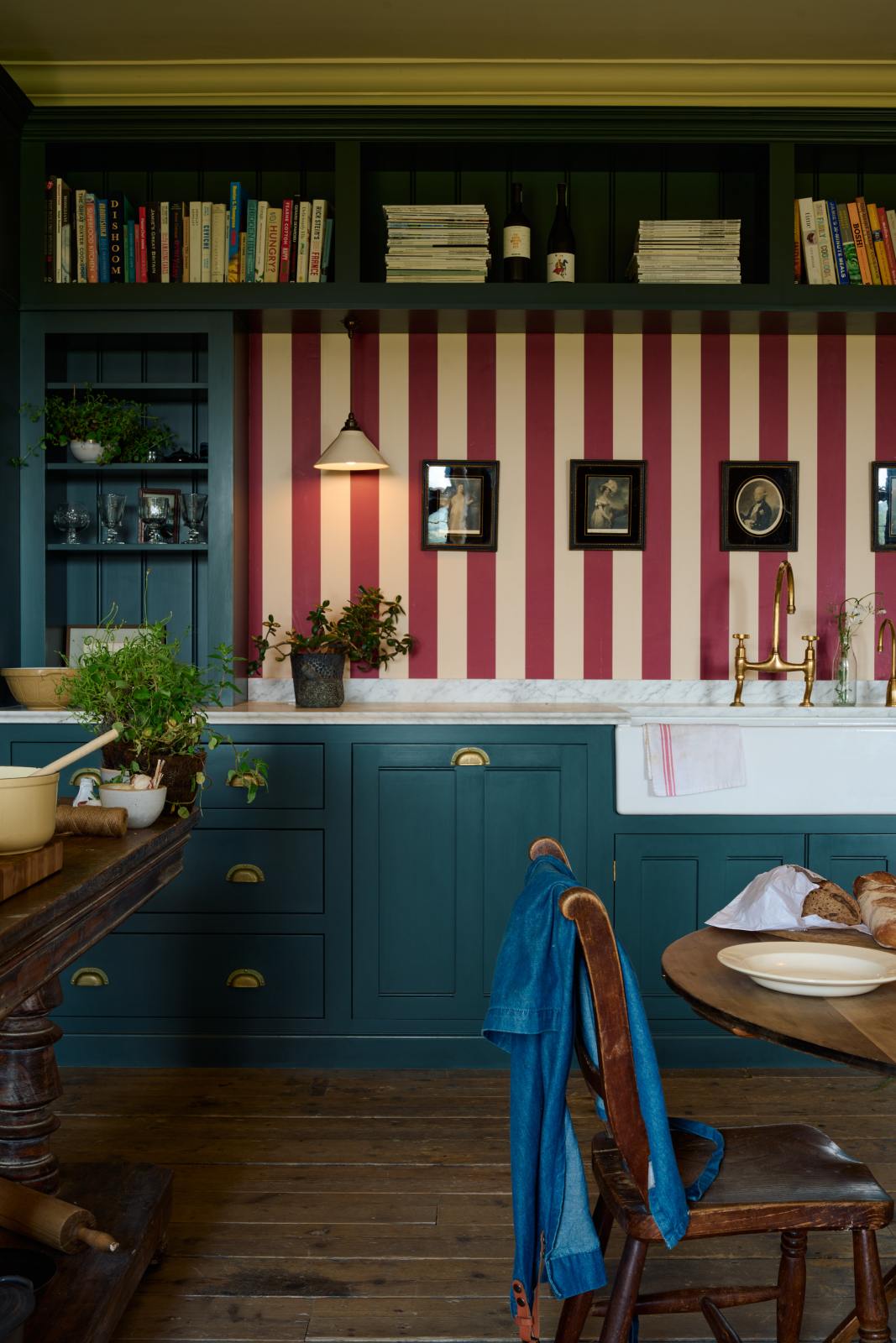 A lovely modern kitchen that retains the charm of its original structure and flooring, using the three primary colours in a muted, mature palette. The spacious kitchen features Clerkenwell Blue full-height pantry cabinet, a long sink run with a marble worktop, an open countertop cabinet, a high shelf, and a red-and-white striped splashback.