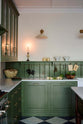 A closer look at a spacious and elegant Wilkes green classic English kitchen, long L-shaped cooker and sink run with a Silestone worktop, glazed wall cupboards, shelves, and Heirloom dairy table. Adorned with classic marble chequered-board flooring, Heirloom task lights, vintage ceramics, copper pots, and luscious green vegetables, it creates a classic and stylish kitchen.