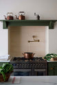A closer look at a spacious and elegant Wilkes green classic English kitchen featuring the gas stove in the chimney breast. Adorned with an aged brass pot filler tap, cream subway splashback tiles, a copper pot, and luscious green vegetables, it embodies a classic and stylish aesthetic.