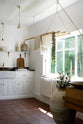 An oblique view of a simple and functional linen white scullery room with a modest sink run with polished sapele, a large single Carrara marble sink, and aged brass Mayan taps. The warm reds and browns of the terracotta square tiles, vintage furniture, ceramics, and a deVOL laundry maid serve the room with both a purpose and beautiful aesthetics.