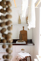 Looking through white lace cloths and a giant wooden rosary hanging on a deVOL laundry maid, is a simple and functional linen white scullery room with a modest sink run with polished sapele, a large single Carrara marble sink, and aged brass Mayan taps. The warm reds and browns of the vintage furniture and ceramics serve the room with both a purpose and beautiful aesthetics.