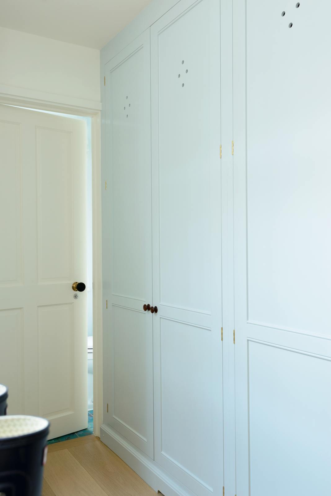 In a bright corridor, the pale-blue coat room features a fitted storage cupboard and shoe shelves, adorned with muddy boots. This simple arrangement adds a touch of character while maintaining a functional and tidy appearance.