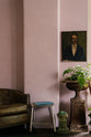 A serene corner of a pastel-colored classic kitchen is beautifully adorned with vintage furniture, including an armchair, a stool, garden ornaments, vibrant plants, and an oil painting.