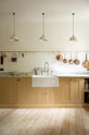 This charming blush yellow, classic English kitchen features a Carrara marble countertop, an ornate backsplash, and an aged brass tap. Decorated with copper pots, vintage ceramics, and small wooden cleaning supplies, it creates an elegant and tidy atmosphere.