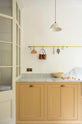 A charming blush yellow, classic English kitchen features a Carrara marble countertop, an ornate backsplash, and a porcelain pendant light. Decorated with copper pots, vintage ceramics, and small wooden cleaning supplies, it creates an elegant and tidy atmosphere.