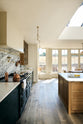 Nestled between the elegant and spacious Haberdasher’s kitchen, which features a large cooker run and a kitchen island with an Arabescato marble worktop, splashback, and glazed cupboards, is a long window wall that lets in bright white light. Adorned with vintage furniture, artisan ceramics, glass flower pendant lights, and a sunflower arrangement, this kitchen creates a classic social space with functional storage.